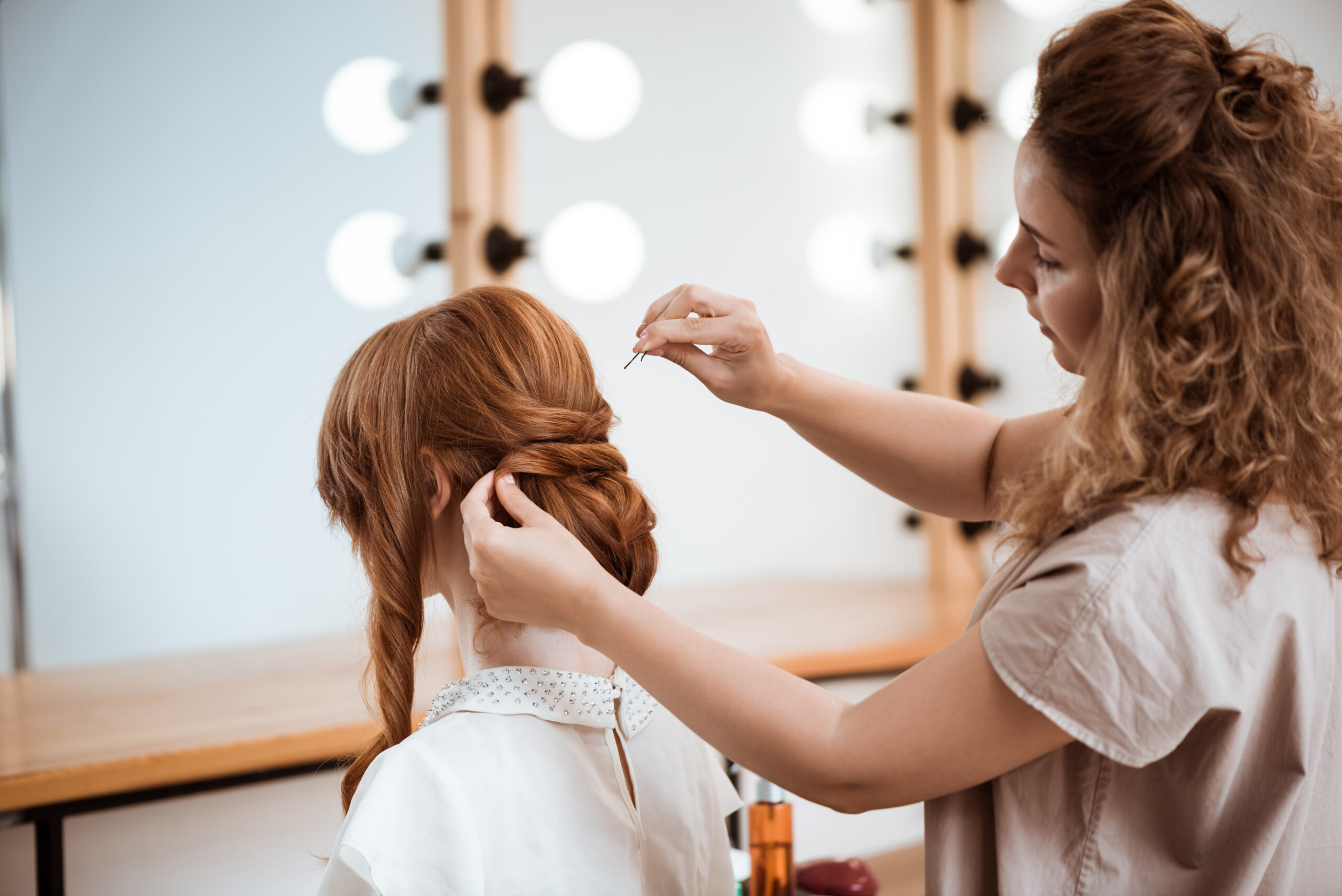 Female hairdresser making hairstyle to redhead girl in beauty salon.